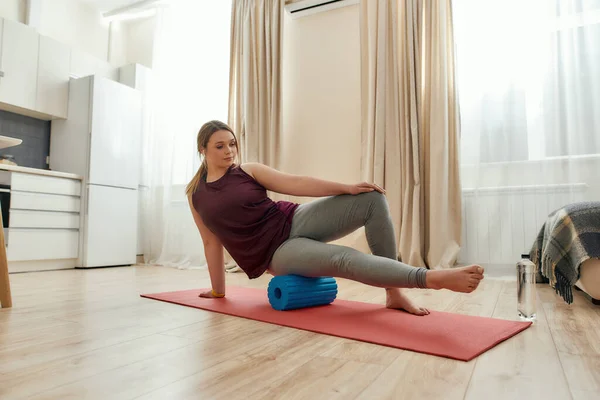 Your steps to fitness. Full length shot of young curvy woman in sportswear exercising using foam roller on a yoga mat at home