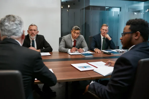 Un asunto serio. Cinco personas de negocios multiculturales en ropa formal discutiendo tener una reunión en la oficina moderna — Foto de Stock