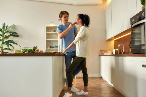 Come sano. Foto completa de pareja feliz, vegetarianos cocinando el desayuno en la cocina. Mujer degustando sándwich que hicieron juntos. Vegetarianismo, comida saludable, dieta, quedarse en casa concepto — Foto de Stock