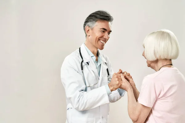 ありがとうございます先生。先輩患者の手を握り笑顔で医療制服姿の朗らかな男性医師。サイドビュー — ストック写真