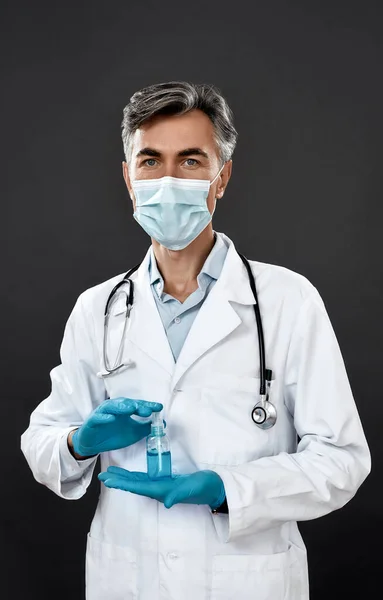 Tıbbi üniformalı profesyonel bir erkek doktor. Steteskop boynunda antiseptik jel tutarken siyah arka planda duruyor. — Stok fotoğraf