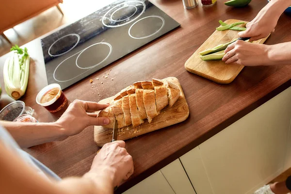 Vágott lövés pár vágás ízletes házi kenyér és szeletelés uborka, miközben az egészséges étel a konyhában együtt. Vegarianizmus, egészséges étel koncepció — Stock Fotó