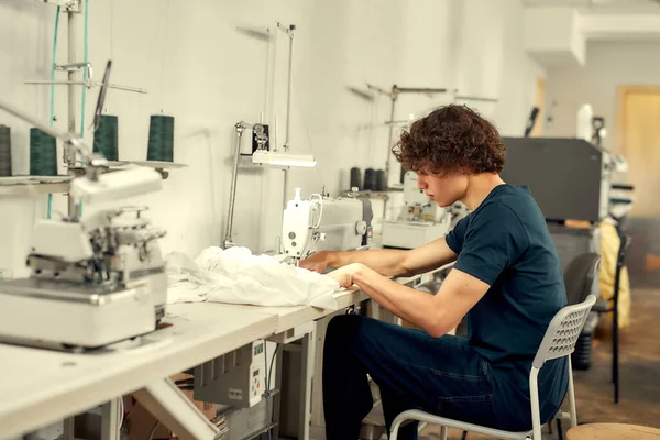 Uwielbiam twoją kreatywność. Młody człowieku, projektant odzieży siedzi i szyje. Dressmaker pracuje nad maszyną do szycia. Krawiec szyjący odzież w miejscu pracy — Zdjęcie stockowe