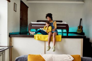 Okumak hayal gücünü besler. Afro-amerikan bebek bakıcısı ve beyaz kız kitap okuyor, evde otururken peri masalı gibi. Çocuk eğitimi, boş zaman aktiviteleri, bebek bakıcılığı konsepti