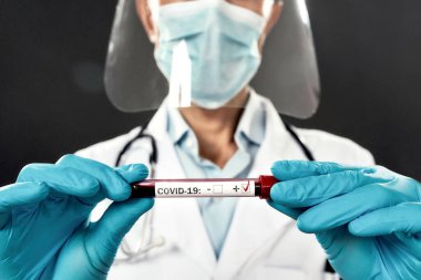 Yüz kalkanı ve mavi eldivenli erkek doktor COVID-19, Coronavirus için pozitif kan testi sonuçları gösteriyor. Bir test tüpüne seçici odaklanma