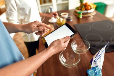 En iyi tarifler. Kadın smoothie hazırlarken adam tarifi tablet bilgisayarla kontrol ediyor. Vejetaryenler mutfakta birlikte yemek pişiriyor. Vejetaryenlik, sağlıklı yiyecekler, diyet, evde kalma kavramı