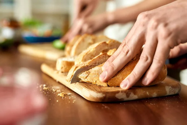Close up de mãos masculinas cortando saboroso pão caseiro na tábua de madeira. Vegetarianismo, conceito de alimentação saudável . — Fotografia de Stock