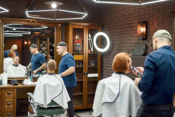 Dwóch fryzjerów pracujących z klientami w nowoczesnym salonie fryzjerskim — Zdjęcie stockowe