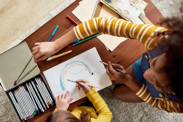 Kreativität. Draufsicht auf ein kaukasisches kleines Mädchen, das Zeit mit einer afrikanisch-amerikanischen Babysitterin verbringt. Sie ziehen eine Maus zusammen — Stockfoto