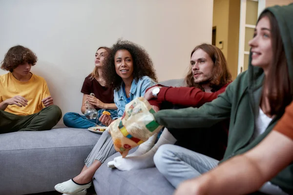 Group of teenagers eating snacks and talking while having fun, relaxing together, sitting on the coach at home — Stock Photo, Image