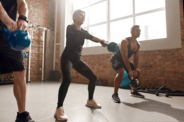 Sağlam bir vücut. Endüstriyel spor salonunda antrenman yaparken kilo alan neşeli atletik kadın. Grup eğitimi, takım çalışması konsepti