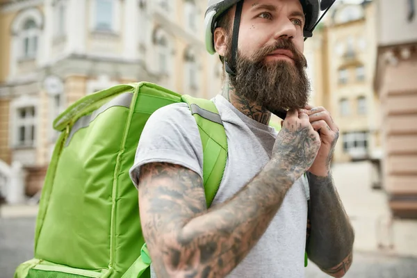 在户外带着保暖袋或背包站着，准备骑自行车的时候，紧紧地抱着一个带着头盔、凶残胡子的送货人。快递、送货服务概念 — 图库照片