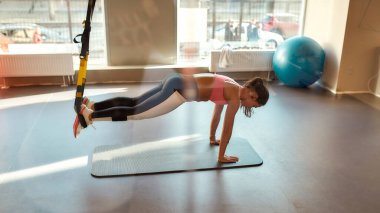 Spor salonundaki spor kemerlerini kullanarak vücudunu esneten genç bir kadın. Spor, sağlıklı yaşam tarzı konsepti