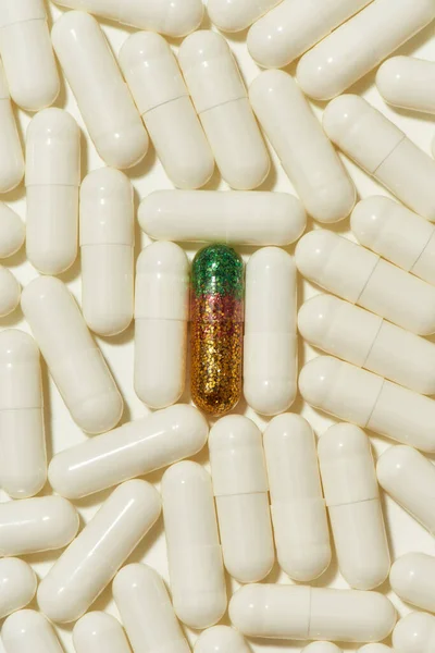 Vista dall'alto di verde pillola glitter dorato che giace al centro tra le altre pillole bianche, capsule. Assistenza sanitaria, idea creativa e concetto di soluzione — Foto Stock