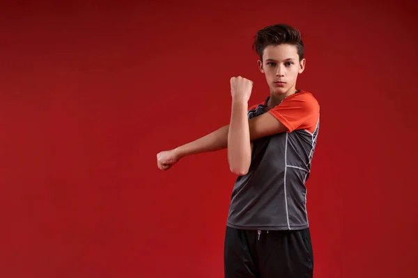 Hora de actuar. Un adolescente se dedica a la aptitud física, está mirando a un lado mientras hace ejercicio. Aislado sobre fondo rojo. Deporte, entrenamiento, fitness, concepto de estilo de vida activo. Disparo horizontal — Foto de Stock