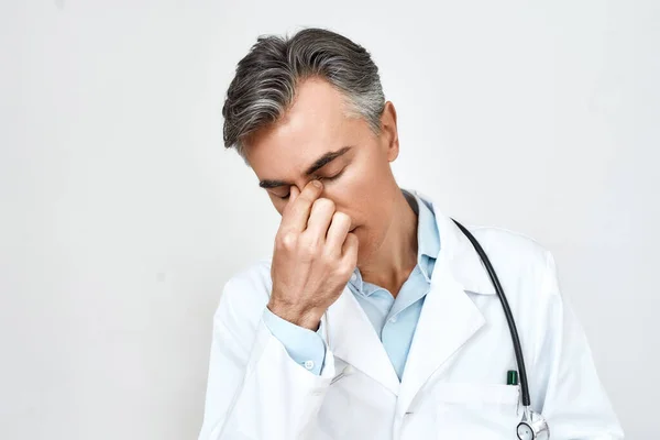 Portré fáradt stresszes férfi orvos orvosi egyenruha érzés ideges, szem csukva és megható orr, miközben áll szemben szürke háttér — Stock Fotó