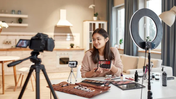 Este es el futuro. Blogger asiática mostrando productos cosméticos mientras graba un video tutorial para su blog de belleza usando cámara en casa —  Fotos de Stock