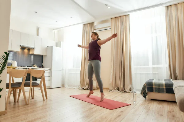 Haciendo más posible. Tiro de cuerpo entero de mujer joven con curvas en ropa deportiva ejercitándose sobre una esterilla de yoga en casa — Foto de Stock