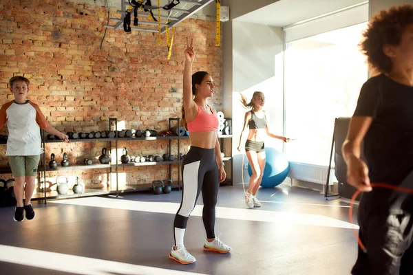 Fornire una vita sana. Colpo pieno di controllo trainer femminile, prendersi cura dei bambini, mentre stanno saltando corda in palestra. Sport, vita sana, educazione fisica — Foto Stock