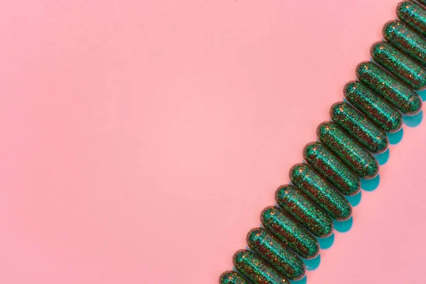 Creatief concept met veel groene glitter pillen liggend diagonaal in een rij geïsoleerd op pastelroze achtergrond. Minimale stijl, kunstconcept — Stockfoto