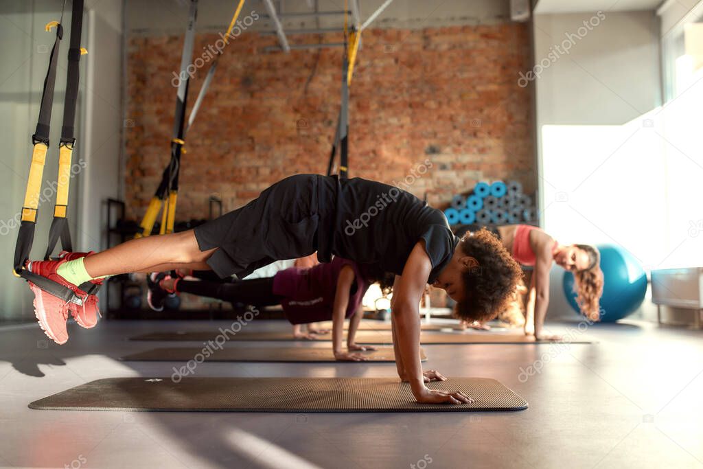 Teenage kids doing exercises on mat using fitness straps in gym with female trainer. Sport, healthy lifestyle, physical education concept