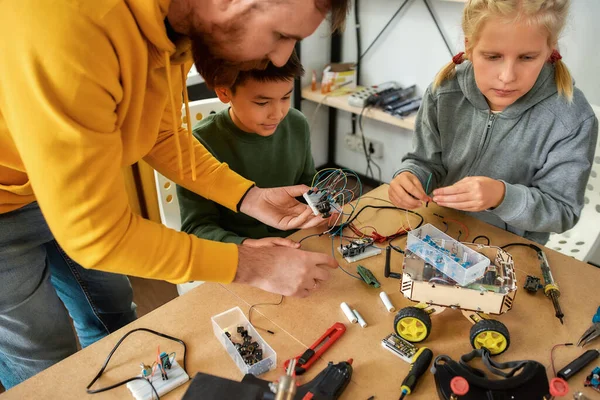 Hacerlo realidad. Captura recortada de técnicos jóvenes construyendo un robot, trabajando con un kit de cableado junto con un profesor masculino en una clase de robótica de vástago. Invenciones y creatividad para niños —  Fotos de Stock