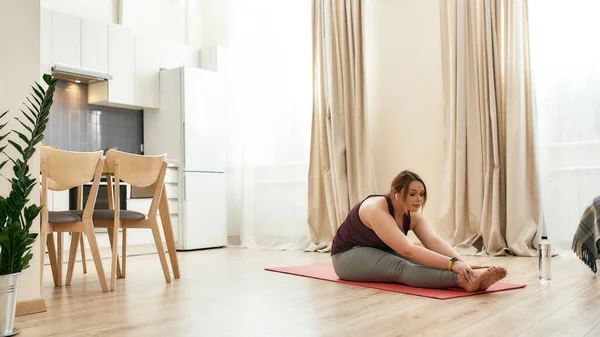 Siktir git. Spor kıyafetli, kablosuz kulaklık kullanan, yoga minderinde egzersiz yapan genç bir kadın. — Stok fotoğraf