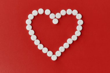 Kırmızı arka planda beyaz haplardan yapılmış kalbin üst görüntüsü. Kalp ve kardiyovasküler hastalıklar, sağlık ve tedavi kavramı