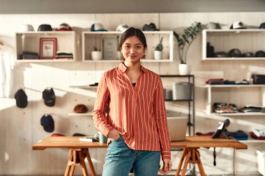 Yaratıcılığa hazır. Ofiste dikilirken kameraya bakan gülümseyen genç bayan işçinin portresi. Özel tişört ve giysi baskı şirketinde çalışan bir kadın.