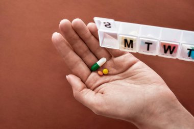 Pazar günü için haftalık bir ilaç kutusu açılmış. Terracotta arka planında beyaz hap kutusundan alınan el hapları ve vitaminler. Sağlık, vitamin ve tedavi kavramı