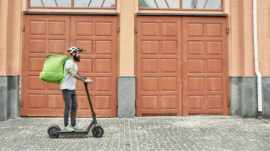 Deneyimi hisset. Kasklı, termal çantalı ya da sırt çantalı sakallı bir teslimatçı şehirde elektrikli scooter 'a binip yiyecek getiriyor. Kurye, teslimat hizmeti konsepti