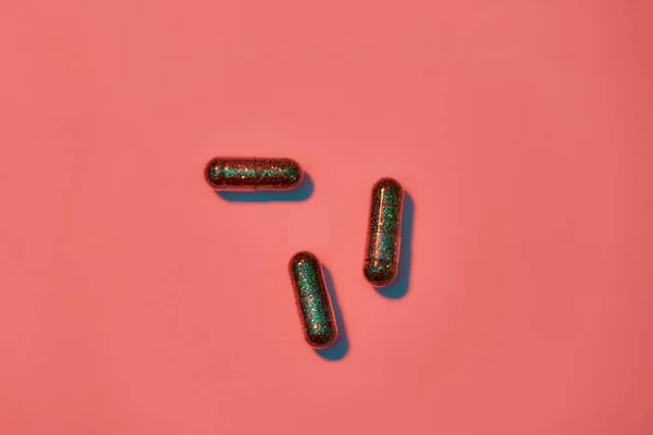 Concetto creativo con pillole glitter verdi su sfondo rosa pesca. Stile minimale . — Foto Stock