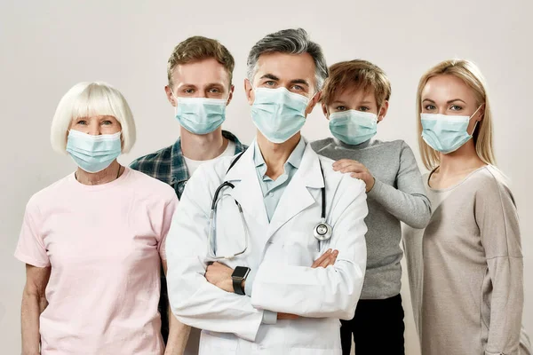 Aile Hekimi. Tıbbi koruyucu maskeler takan dört çocuklu yetişkin erkek doktor ve aile portresi gri arka planda kameraya bakıyor. — Stok fotoğraf