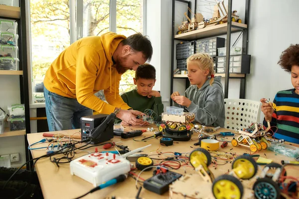 Решение всех проблем. Молодые техники строят робота, работают с комплектом электропроводки вместе с учителем-мужчиной в классе стебельной робототехники. Изобретения и творчество для детей — стоковое фото