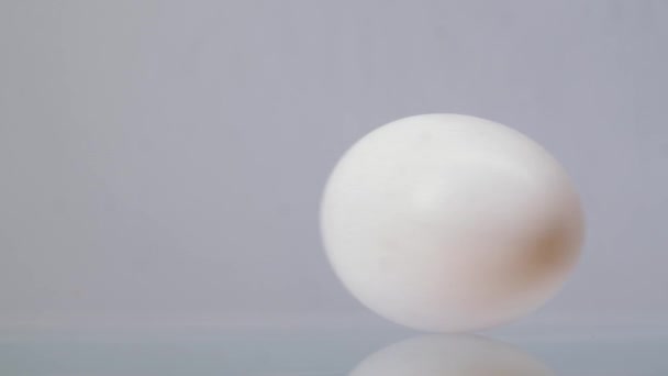 Œuf de poulet blanc tournant autour et roulant sur un fond blanc avec une belle réflexion