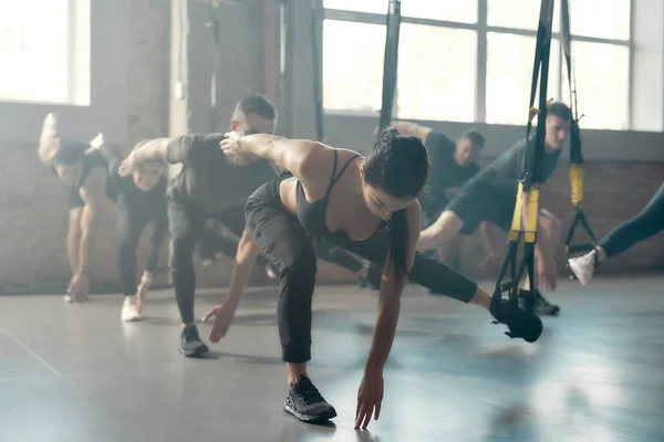 Centre de fitness. Portrait d'hommes et de femmes faisant des exercices de fitness dans une salle de gym industrielle. Sangles, concept d'entraînement de groupe — Photo