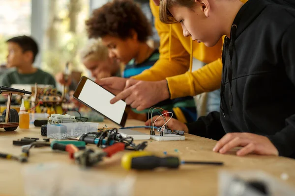 Fikirlerimizi paylaşıyoruz. Kök robotik dersinde kablo takımıyla çalışan genç teknisyenlerin görüntüsü. Erkek öğretmen onlara yardım ediyor, tavsiye veriyor, tablet bilgisayar kullanıyor. Çocuklar için icatlar ve yaratıcılık — Stok fotoğraf