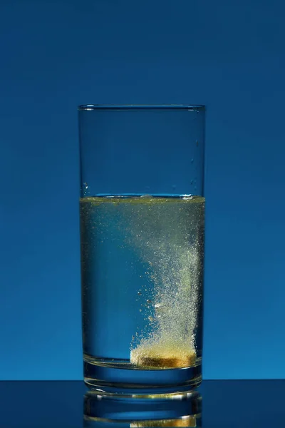 Close-up de vidro de água com comprimido de aspirina efervescente, pílula nele isolado sobre fundo azul. Conceito de saúde — Fotografia de Stock