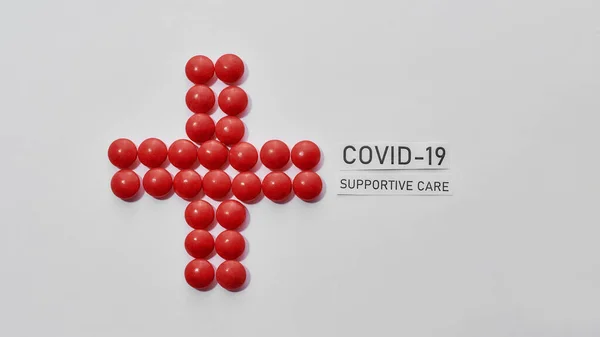 Top view of cross made of red pills and inscription Covid 19 Supportive Care on light background. Medications, virus and treatment concept — Stock Photo, Image