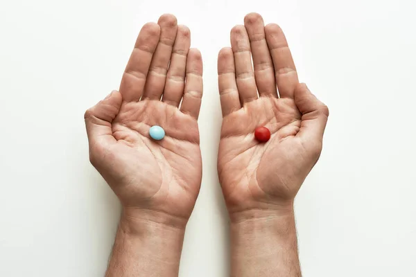 Visão superior da pílula azul em uma mão e pílula vermelha em outra sobre fundo branco. Conceito de escolha e tratamento — Fotografia de Stock