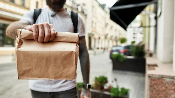 Gehakt schot van de bezorger met papieren zak, terwijl het weggeven van bestelling aan een klant. Koerier, bezorgservice concept — Stockfoto