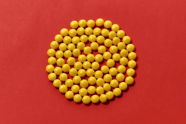 黄色の錠剤は、赤い背景の上に隔離された円の形に横たわっています。ヘルスケアと治療の概念. — ストック写真