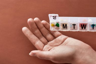 Pazar günü için beyaz ilaç kutusundan haplar ve vitaminler alarak terracotta arka planında haftalık ilaç kutusu açıldı. Sağlık, vitamin ve tedavi kavramı