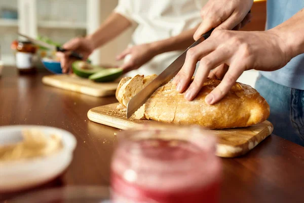 Férfi kezek vágás ízletes házi kenyeret a fa fórumon. A fiatal pár egészséges ételt készít együtt a konyhában. Vegarianizmus, egészséges étel koncepció. — Stock Fotó