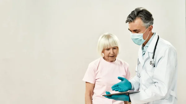 Γιατρός και ασθενής. Ώριμος άνδρας γιατρός με ιατρική στολή και προστατευτική μάσκα που εξηγεί τη διάγνωση σε ηλικιωμένη γυναίκα ασθενή — Φωτογραφία Αρχείου