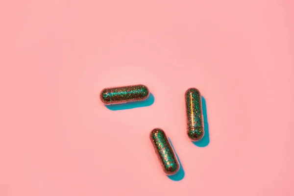 Concetto creativo con pillole glitter verdi isolate su sfondo rosa pastello. Stile minimale, concetto di arte — Foto Stock