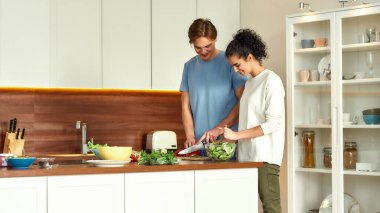 Kadın salata fırlatırken, genç adam sebze kesiyor. Vejetaryenler mutfakta birlikte sağlıklı yemek hazırlıyorlar. Vejetaryenlik, sağlıklı gıda konsepti.