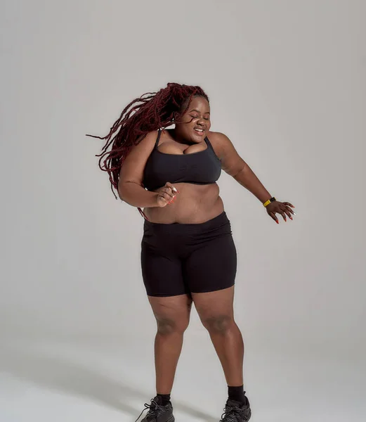 Mein Körper nichts von deiner Sache. Plump, plus size afrikanisch-amerikanische Frau in Sportbekleidung, die Spaß hat, im Studio vor grauem Hintergrund tanzend — Stockfoto