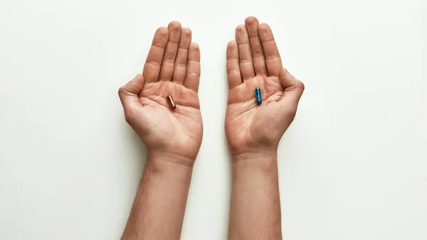 Visão superior da pílula glitter vermelha em uma mão e pílula glitter azul em outra sobre fundo branco. Conceito de escolha e criatividade — Fotografia de Stock