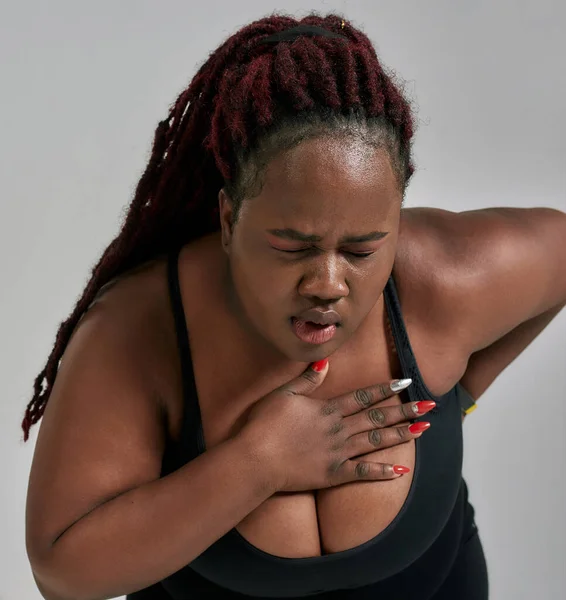 Schmerz. Nahaufnahme einer molligen, plus size afrikanisch-amerikanischen Frau in Sportbekleidung, die müde, erschöpft wird, Schmerzen nach dem Training im Studio vor grauem Hintergrund verspürt — Stockfoto